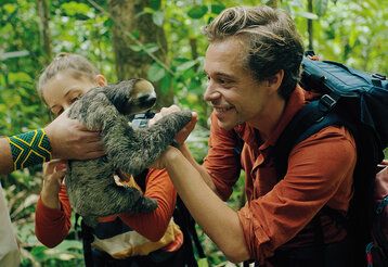 Checker Tobi im Dschungel, ihm wird ein Faultier hingehalten