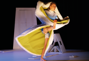 Eine Tänzerin umhüllt von einem gelben Umhang mit Fell tanzt barfuß auf der Bühne