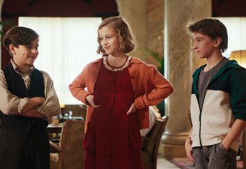 Szene aus dem film Das geheime Stockwerk, drei Kinder stehen in einem nostalisch eingerichteten Salon