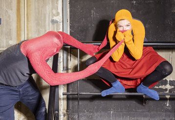 Schauspieler und Schauspielerin tragen Strumpfhosen über den Köpfen und spielen miteinander