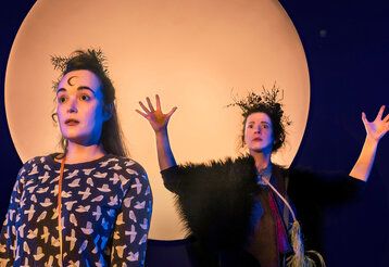 zwei Schauspielerinnen vor einem großen hellen Kreis, der den Mond darstellt