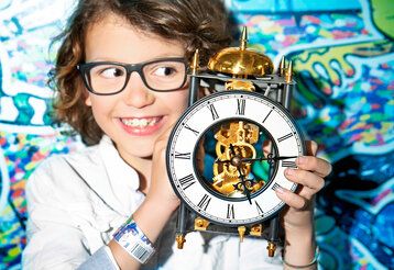 Mädchen mit großem Wecker vor einer bunten Wand