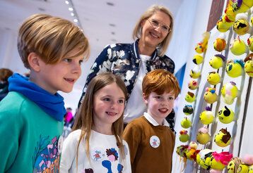 Drei Kinder der Klasse 2b der St. Mauritius Schule und eine Frau stehen vor einem Kunstwerk, das aus Tennsibällen besteht