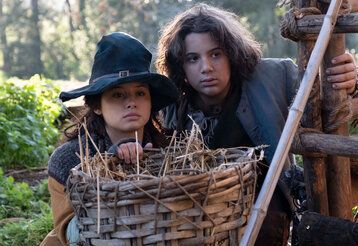 Mädchen mit Hexenhut und Junge in mittelalterlicher Kleidung hinter Weidenkorb, draußen