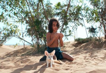 Ein Kind und ein Wüstenfuchs sitzen zusammen im Wüstensand