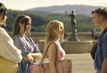 drei junge Frauen stehen einem jungen Mann gegenüber, im Hintergrund eine historische Skulptur und Landschaft