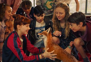 einige Schulkinder hocken beieinander, in ihrer Mitte ein Fuchs