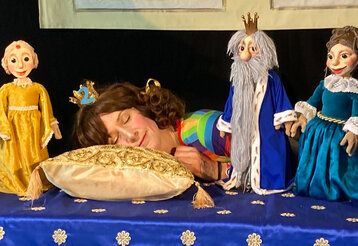 Frau mit Krone liegt auf Kissen aud schläft, daneben kleine Puppen, König und zwei Frauen