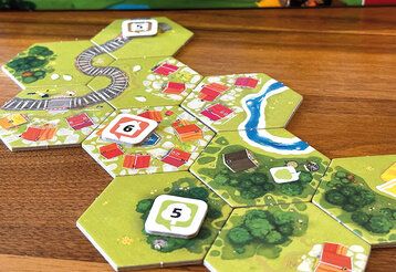 Spielszene von Dorfromantik, sechseckige Spielkarten liegen auf einem Tisch