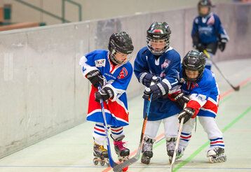 Drei Kinder spielen Inlineskate-Hockey