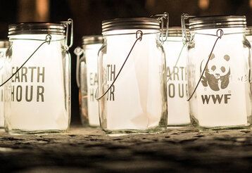 leuchtende Einmachgläser mit dem Schriftzug Earth Hour und dem WWF-Logo im Dunklen, im Hintergrund unscharf: das Brandenburger Tor