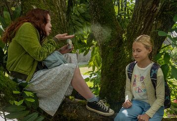 Szene aus dem Film Ein Mädchen namens Willow, zwei Mädchen sitzen auf einem Baum, das eine pustet etwas von seiner Hand zu dem anderen Mädchen