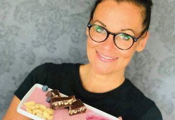 Porträt von Anja Hohmann, die einen eckigen Teller mit Schokolade, Cashewkernen und Blaubeeren hält