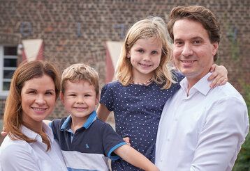 Familie Groß vor einem Haus in Unterrath, die Mutter hat den Sohn auf dem Arm und der Vater trägt die Tochter