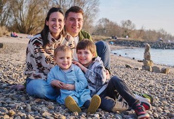 Porträt der Familie Hefer-Davis, Mutter, Vater und zwei Kinder sitzen am Rhein in Himmelgeist