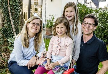 Vater, Mutter und zwei Töchter im Garten, ein Mädchen sitzt auf der Schaukel