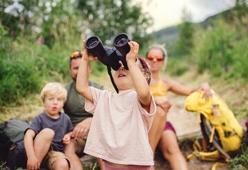 Familie macht Rast bei einer Wanderung, kleines Mädchen guckt in ein Fernglas
