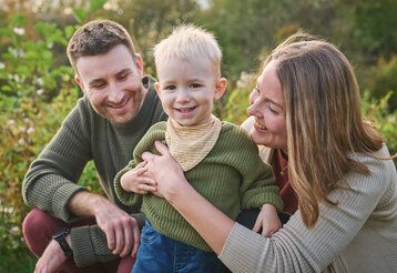 Vater, Mutter mit kleinem Jungen, im Hintergrund Gebüsch