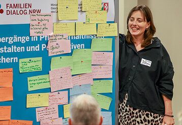 eine Frau steht an einem Stellwand, an der bunte Zettel hängen