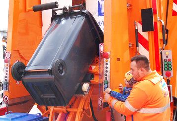 Kleiner Junge und Awista-Mitarbeiter leeren Mülltonne in Müllwagen gemeinsam mit Hydraulik