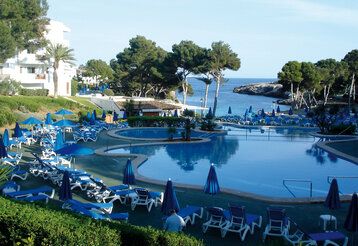 Poolanlage eines Familienhotels auf einer spanischen Insel, im Hintergrund Meer