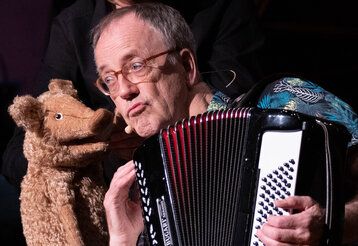 Mann spielt das Akkordeon währen ein Plüschschwein mit ihm spricht
