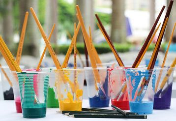 verschiedene Plastikbecher mit bunter Farbe und Pinseln