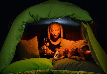 Eine Schauspielerin mit Hasenohren spielt in einer aus Kissen gebauten Höhle mit einer Hasen- und einer Fuchspuppe.