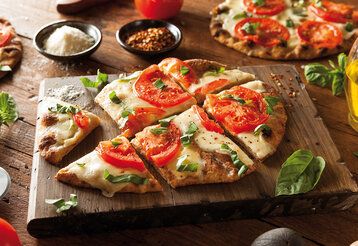 Fladenbrotpizza auf Holzbrett, Zutaten stehen daneben