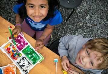 zwei Kinder von oben fotografiert, die mit Lego spielen, beide gucken nach oben
