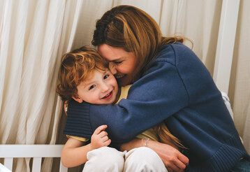 eine Frau knuddelt mit ihren Kind, das schaut lächelnd in die Kamera