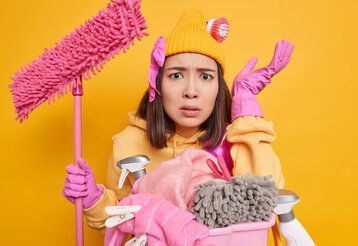 dunkelhaarige Frau mit Wischmopp und Putzzeug vor gelbem Hintergrund