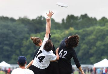Frisbeespieler:innen springen in die Luft und wollen einen Frisbeescheibe fangen, die noch durch die Luft fliegt, man sieht sie von hinten