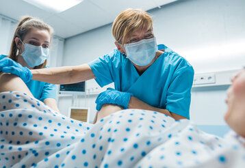 Eine Frau wird bei der Geburt im Kreißsaal von zwei Hebammen betreut
