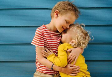 Zwei Jungs umarmen sich, im Hintergrund: blaue Wand