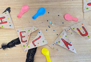 Girlande auf der „Helau“ steht, liegt auf Holzuntergrund, daneben Federn, Luftballons und Pailletten