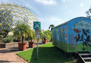 Die Glaskuppel des Botanischen Gartens der HHU Düsseldorf, im Vordergrund ein blauer Bauwagen