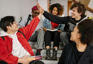 Gruppe Jugendliche sitezn in einem Treppenhaus, zwei machen High Five