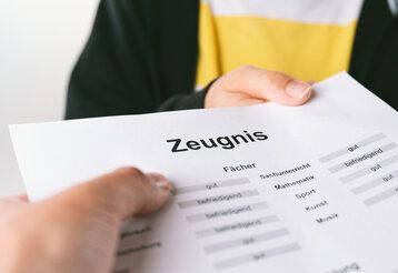 Hand eines Erwachsenen nimmt das Schulzeugnis eines Kindes