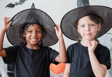 Zwei Mädchen mit schwarzen Hexenhüten gucken in die Kamera