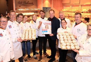 Handwerksbäcker stehen mit Backblechen voller Berliner in einem Verkaufsraum der Bäckerei Behmer