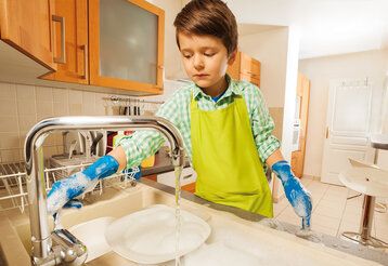 Ein Junge steht mit blauen Gummihandschuhen am Spülbecken und macht den Abwasch