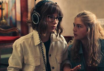 Zwei Mädchen stehen nebeneinander, eine trägt einen Kopfhörer und guckt erstaunt