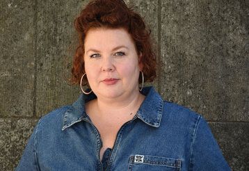 Porträt der Kunstvermittlerin Jana-Catharina Israel vor einer Mauer mit grauen Mauersteinen