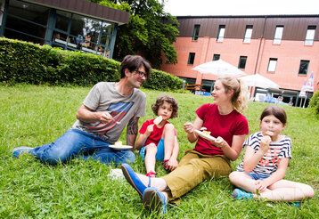 Vater, Mutter und zwei Kinder sitzen auf einem rasen vor der Jugendherberge in Bonn
