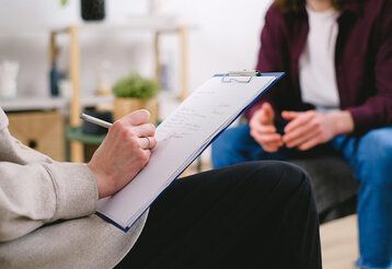 ein Jugendlicher im Beratungsgespräch, im Vordergrund eine Beraterin, die erwas aufschreibt