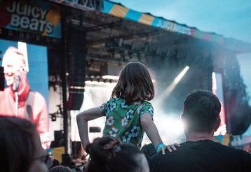 Kind mit Vater im Publikum des Festivals Juicy Beats, im  Hintergrund eine große Bühne