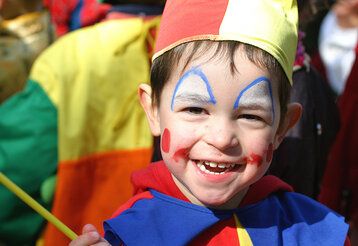 Kleiner Junge, als Clown verkleidet, im Karnevalsgetümmel, lacht in die Kamera