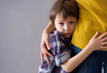 Trauriger Junge schmiegt sich an Mamas Bein