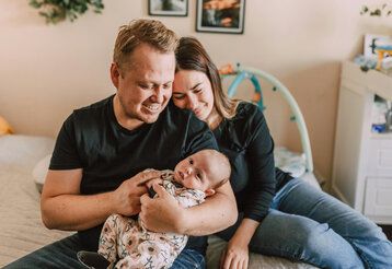 Junge Eltern sitzen mit ihrem Baby auf einem Bett